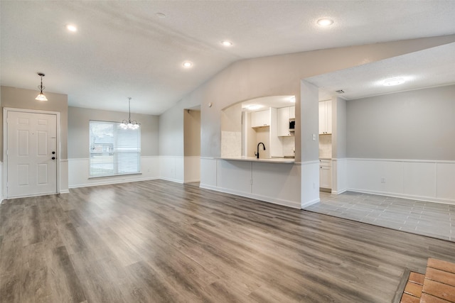 unfurnished living room with sink, a chandelier, vaulted ceiling, a textured ceiling, and hardwood / wood-style floors