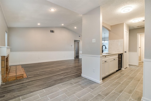 kitchen with sink, white cabinetry, light hardwood / wood-style floors, vaulted ceiling, and beverage cooler