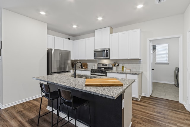 kitchen with sink, stainless steel appliances, light stone counters, white cabinets, and a center island with sink