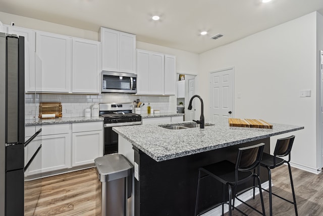 kitchen featuring an island with sink, sink, white cabinets, stainless steel appliances, and light stone countertops