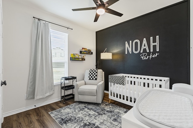 bedroom with a crib, dark wood-type flooring, and ceiling fan