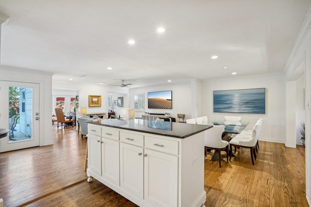 kitchen with white cabinets, a center island, ceiling fan, light hardwood / wood-style floors, and crown molding