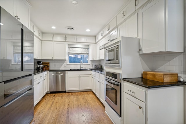 kitchen featuring sink, light hardwood / wood-style flooring, appliances with stainless steel finishes, tasteful backsplash, and white cabinets