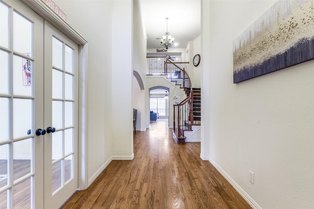 hall with french doors, a towering ceiling, a chandelier, and hardwood / wood-style flooring