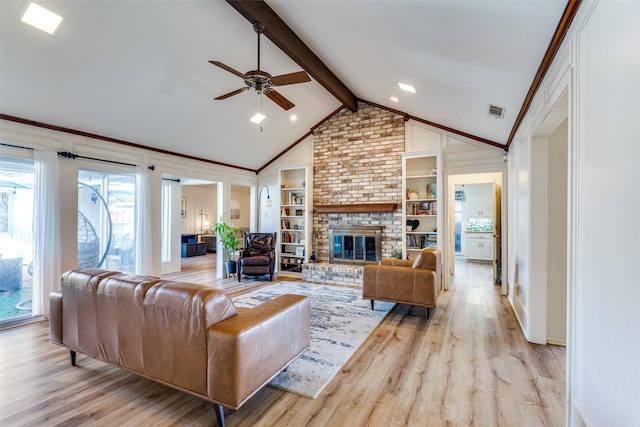 living room with vaulted ceiling with beams, light hardwood / wood-style flooring, ceiling fan, a brick fireplace, and built in shelves