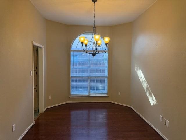 unfurnished room featuring a notable chandelier, baseboards, and wood finished floors