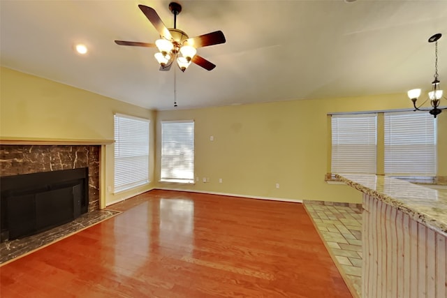 unfurnished living room with ceiling fan with notable chandelier, a high end fireplace, wood-type flooring, and vaulted ceiling