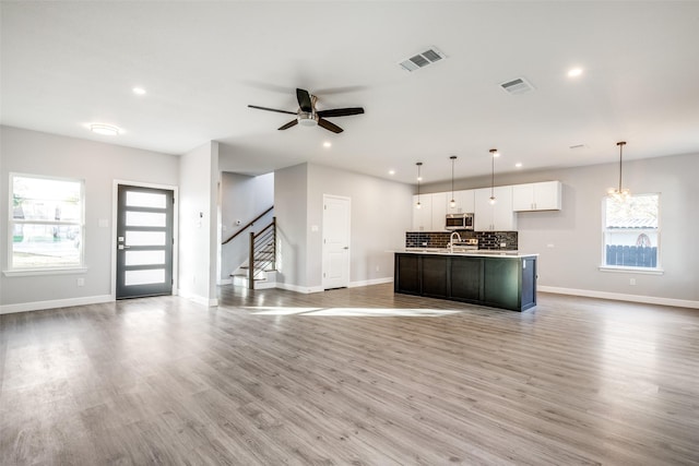 kitchen with white cabinetry, hanging light fixtures, light hardwood / wood-style flooring, an island with sink, and decorative backsplash