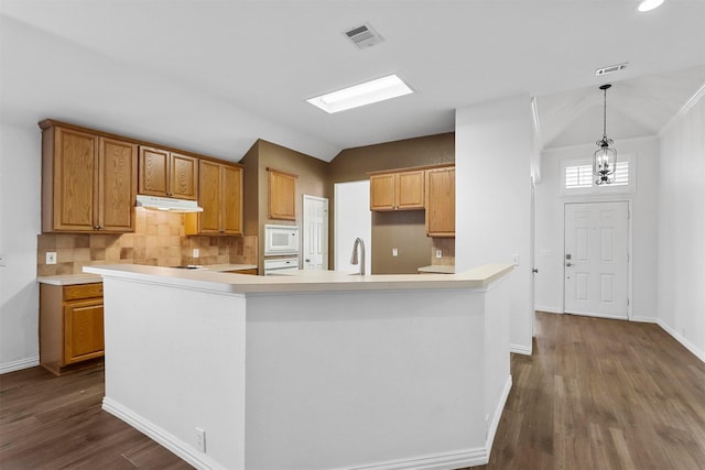 kitchen with pendant lighting, white appliances, a kitchen island with sink, lofted ceiling with skylight, and decorative backsplash