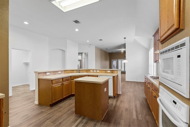 kitchen featuring an island with sink, sink, white appliances, and decorative light fixtures