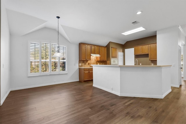 kitchen featuring vaulted ceiling, pendant lighting, white microwave, backsplash, and dark wood-type flooring