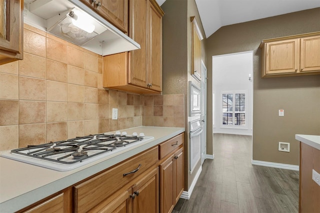 kitchen featuring dark hardwood / wood-style floors, lofted ceiling, backsplash, exhaust hood, and white appliances