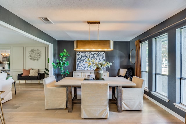 dining area with an inviting chandelier, a textured ceiling, and light hardwood / wood-style floors