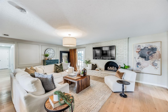 living room featuring a brick fireplace, a textured ceiling, and light hardwood / wood-style flooring