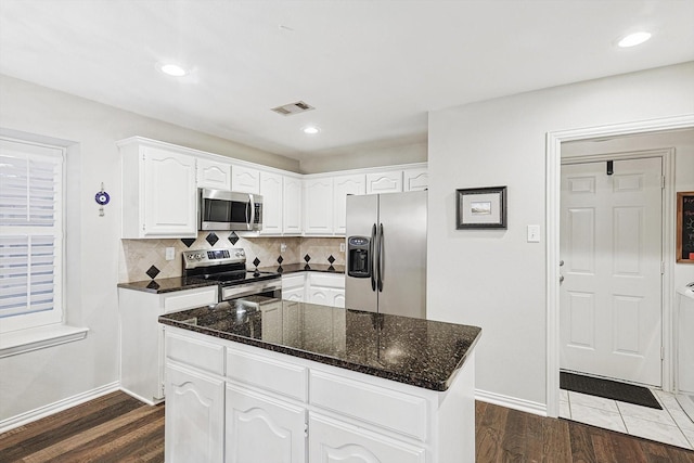 kitchen with appliances with stainless steel finishes, white cabinets, backsplash, a center island, and dark wood-type flooring