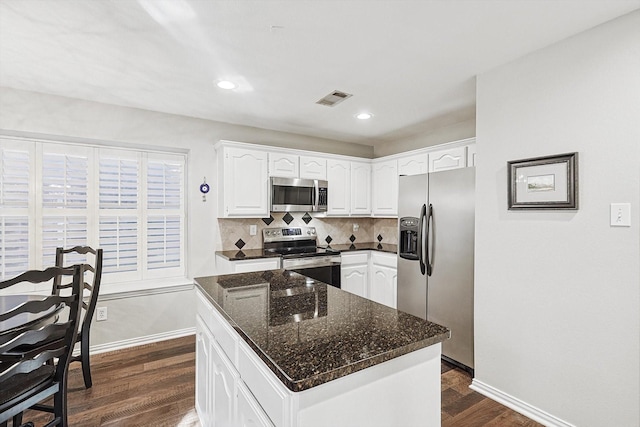 kitchen featuring appliances with stainless steel finishes, dark hardwood / wood-style floors, white cabinetry, dark stone countertops, and a center island