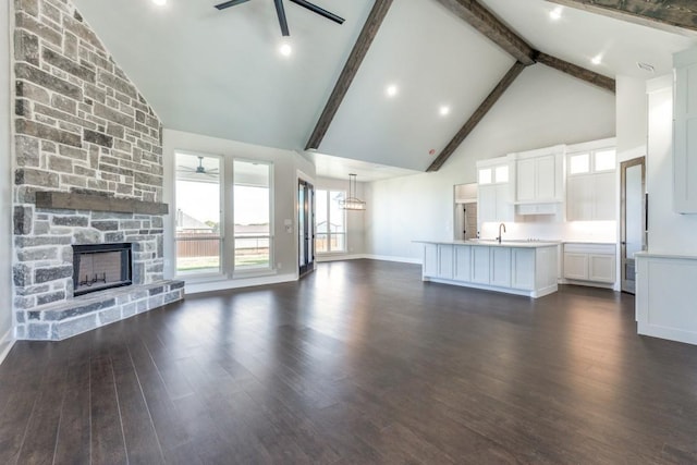 unfurnished living room with a stone fireplace, dark hardwood / wood-style floors, high vaulted ceiling, beamed ceiling, and ceiling fan