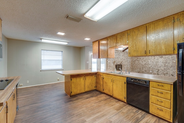 kitchen featuring sink, wood-type flooring, a textured ceiling, black dishwasher, and kitchen peninsula