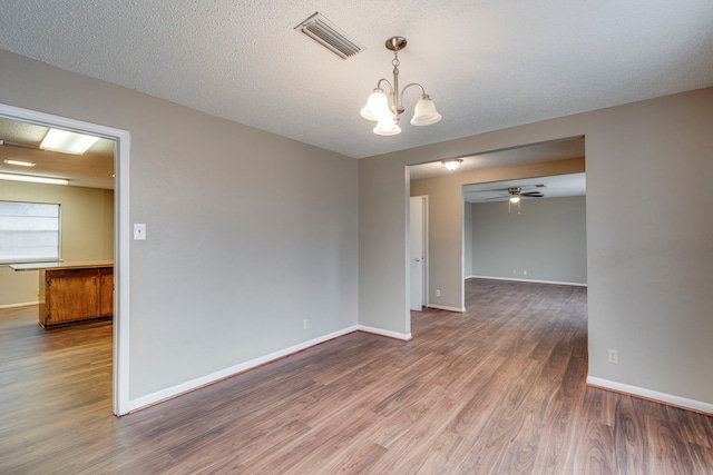 empty room with ceiling fan with notable chandelier, hardwood / wood-style floors, and a textured ceiling