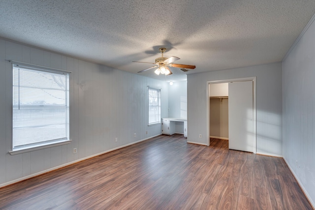 unfurnished bedroom featuring multiple windows, ceiling fan, dark wood-type flooring, and a textured ceiling