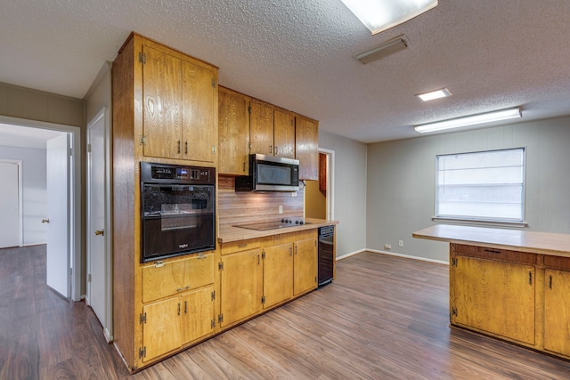 kitchen featuring tasteful backsplash, light hardwood / wood-style flooring, black appliances, and a textured ceiling