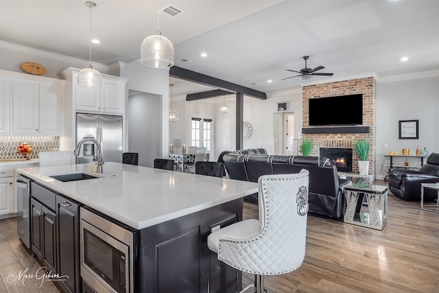 kitchen with a breakfast bar, sink, stainless steel appliances, a kitchen island with sink, and white cabinets