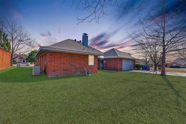 back house at dusk featuring central AC unit, a garage, and a lawn