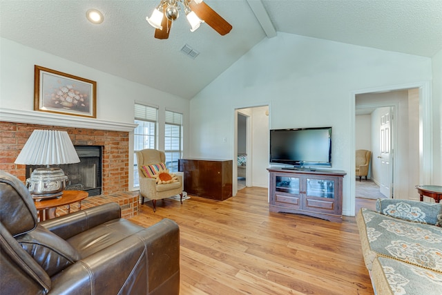 living room with ceiling fan, beam ceiling, a fireplace, a textured ceiling, and light wood-type flooring