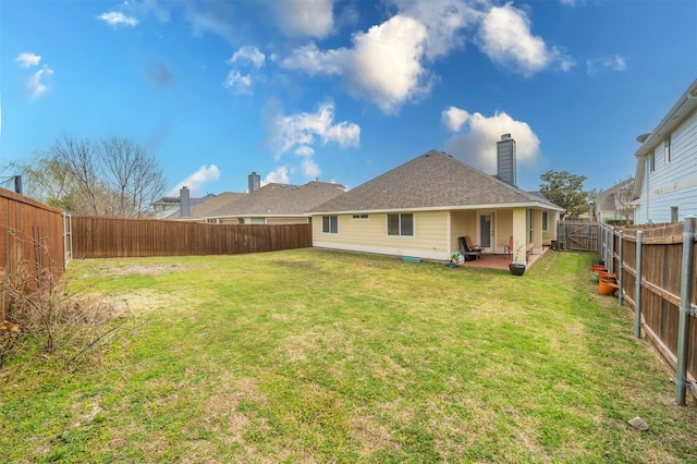 rear view of property featuring a shingled roof, a chimney, a fenced backyard, a yard, and a patio