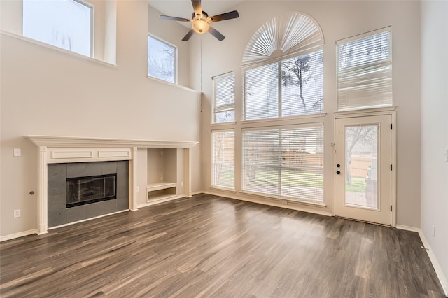 unfurnished living room featuring dark hardwood / wood-style flooring, a tile fireplace, ceiling fan, and a high ceiling