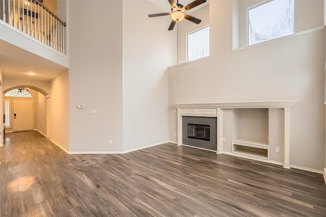 unfurnished living room with ceiling fan, a fireplace, dark hardwood / wood-style floors, and a high ceiling