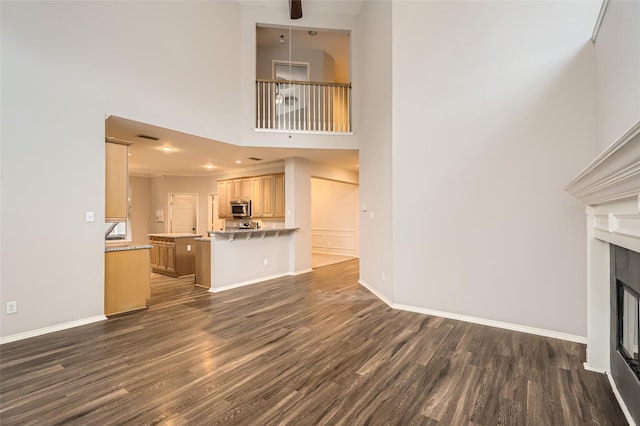 unfurnished living room with a towering ceiling, dark hardwood / wood-style floors, and ceiling fan