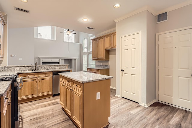 kitchen with a kitchen island, sink, stainless steel appliances, light stone countertops, and light wood-type flooring