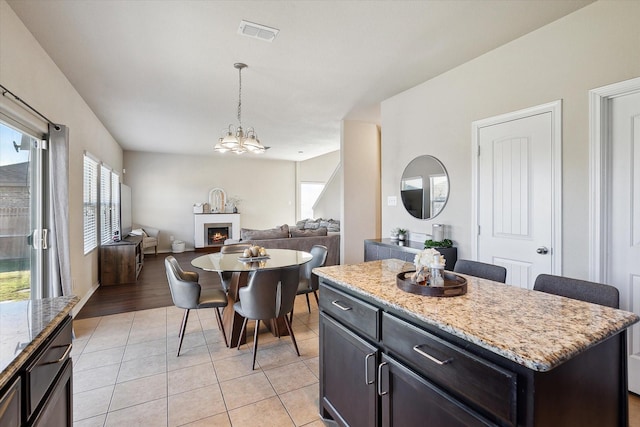 kitchen featuring light tile patterned floors, hanging light fixtures, a center island, light stone counters, and a notable chandelier