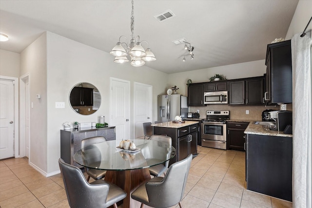 kitchen with light tile patterned floors, appliances with stainless steel finishes, hanging light fixtures, light stone countertops, and a kitchen island