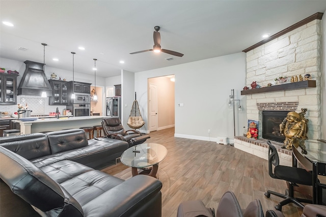 living room with ceiling fan, a stone fireplace, and light wood-type flooring