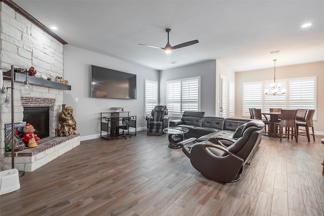 living room with hardwood / wood-style flooring, ceiling fan with notable chandelier, and a large fireplace