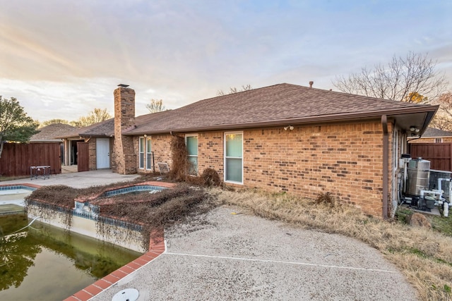 back house at dusk with a pool with hot tub and a patio