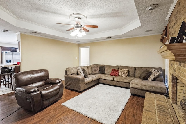 living room featuring a textured ceiling, a tray ceiling, ceiling fan, a fireplace, and hardwood / wood-style floors