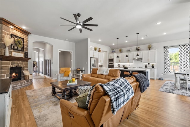 living room with ceiling fan, a stone fireplace, and light hardwood / wood-style flooring