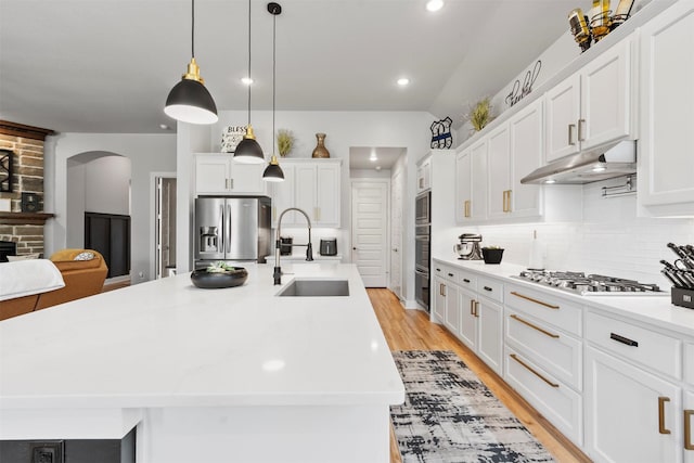 kitchen with appliances with stainless steel finishes, decorative light fixtures, white cabinetry, sink, and a kitchen island with sink