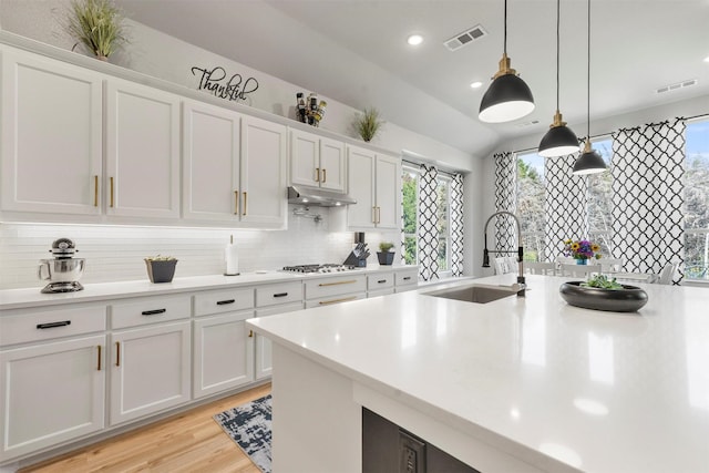 kitchen featuring sink, white cabinetry, decorative backsplash, decorative light fixtures, and stainless steel gas stovetop