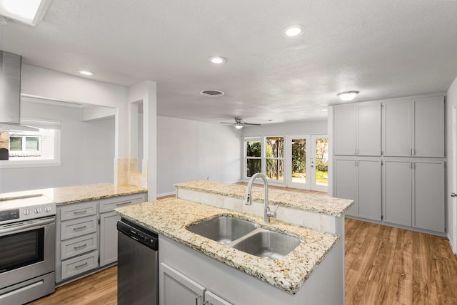 kitchen featuring sink, an island with sink, stainless steel appliances, light stone countertops, and light hardwood / wood-style floors