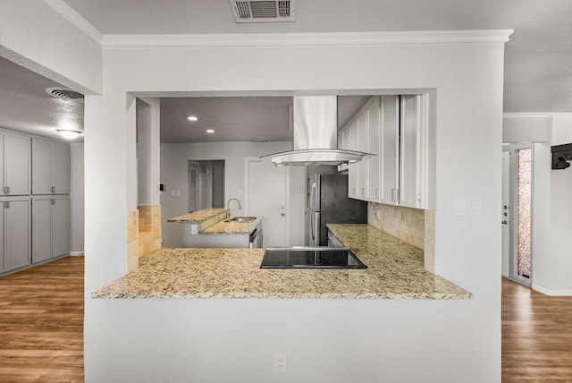 kitchen with crown molding, stainless steel fridge, black electric stovetop, light hardwood / wood-style floors, and island exhaust hood