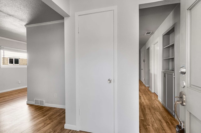 hallway featuring built in shelves, wood-type flooring, and a textured ceiling