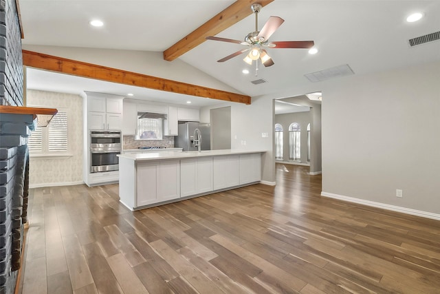 kitchen with hardwood / wood-style flooring, appliances with stainless steel finishes, tasteful backsplash, lofted ceiling with beams, and white cabinets