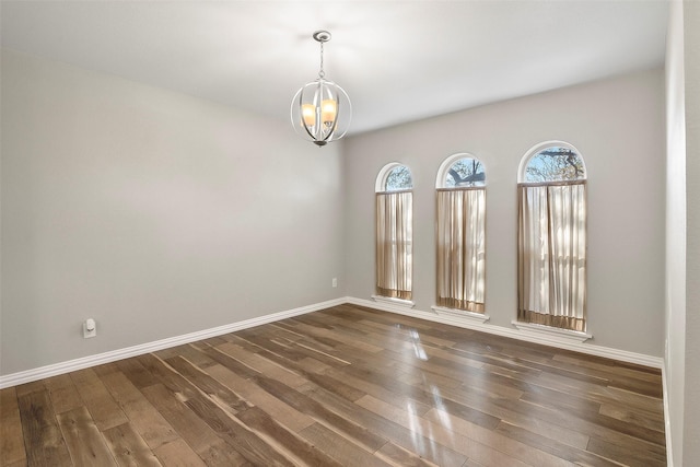 unfurnished room with a notable chandelier and dark hardwood / wood-style floors