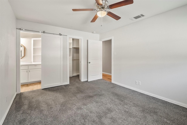 unfurnished bedroom featuring ensuite bathroom, a spacious closet, a barn door, dark carpet, and a closet