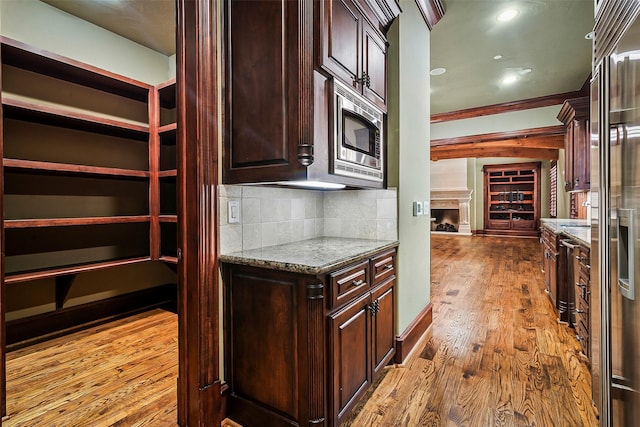 kitchen with light stone counters, built in appliances, light wood-type flooring, ornamental molding, and decorative backsplash