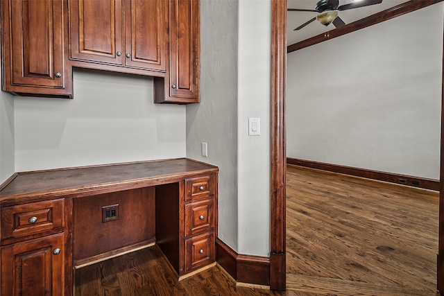 unfurnished office with ceiling fan, built in desk, and dark hardwood / wood-style flooring